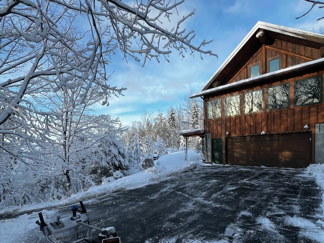 Snow-covered cabin with wooden exterior and large windows, surrounded by winter landscape.