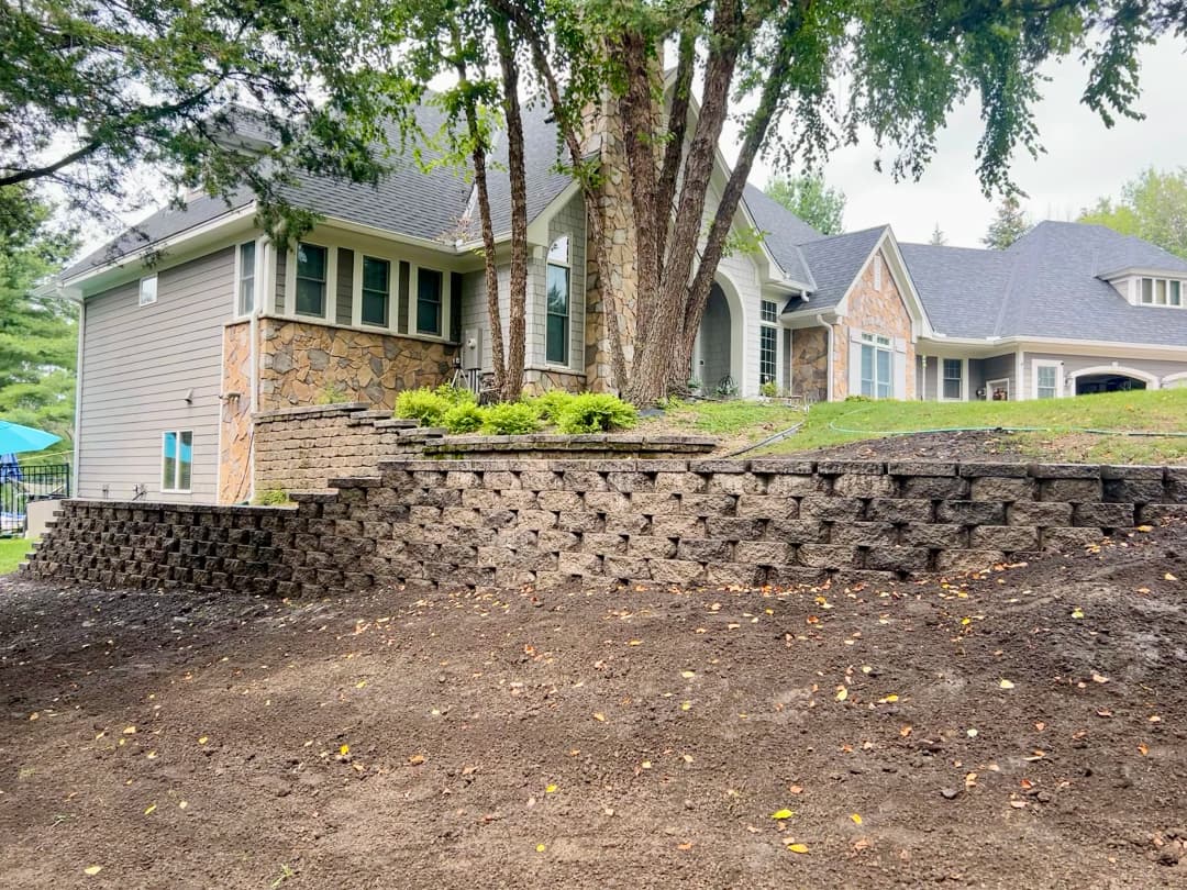 Modern home with stone landscaping and tiered garden in a lush green yard.