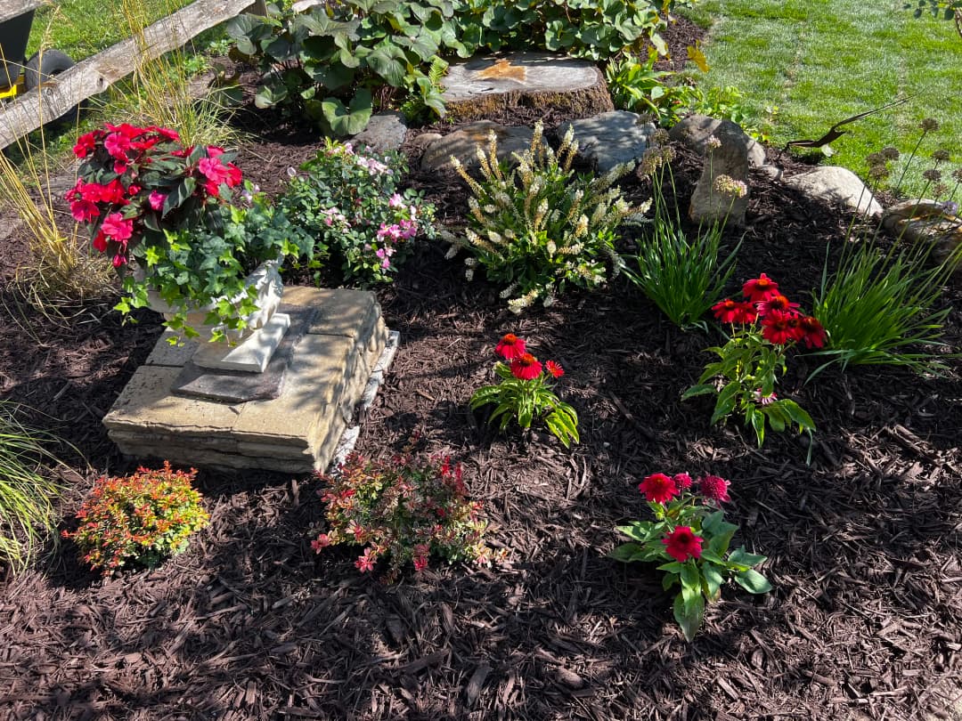 Colorful flower garden with red and pink blooms, stone features, and mulch for landscaping.