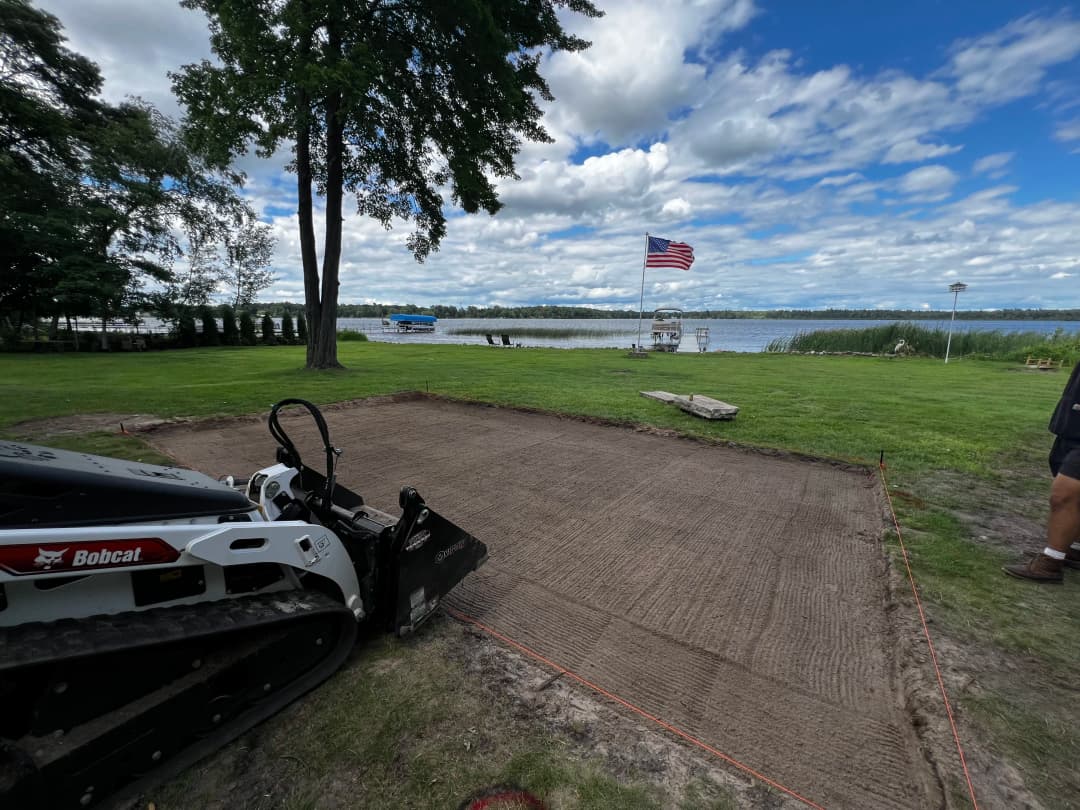 Bobcat skid steer preparing land for a project by a lake with an American flag in the background.