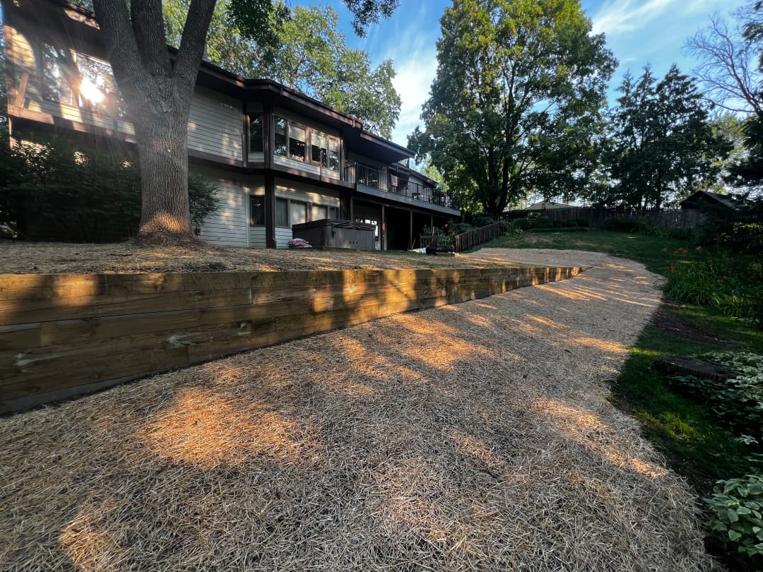 Modern home exterior with landscaped yard, wooden steps, and lush greenery under clear blue sky.