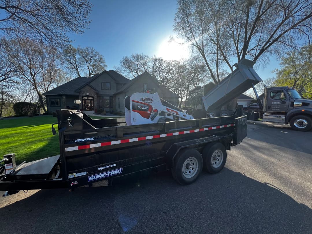 Bobcat MT100 compact track loader on a trailer in front of a residential home.