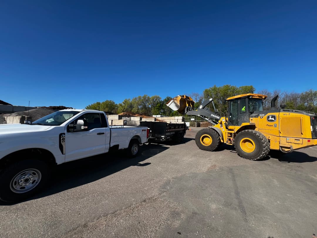 Loader transferring materials to a truck at a construction site under a clear blue sky.