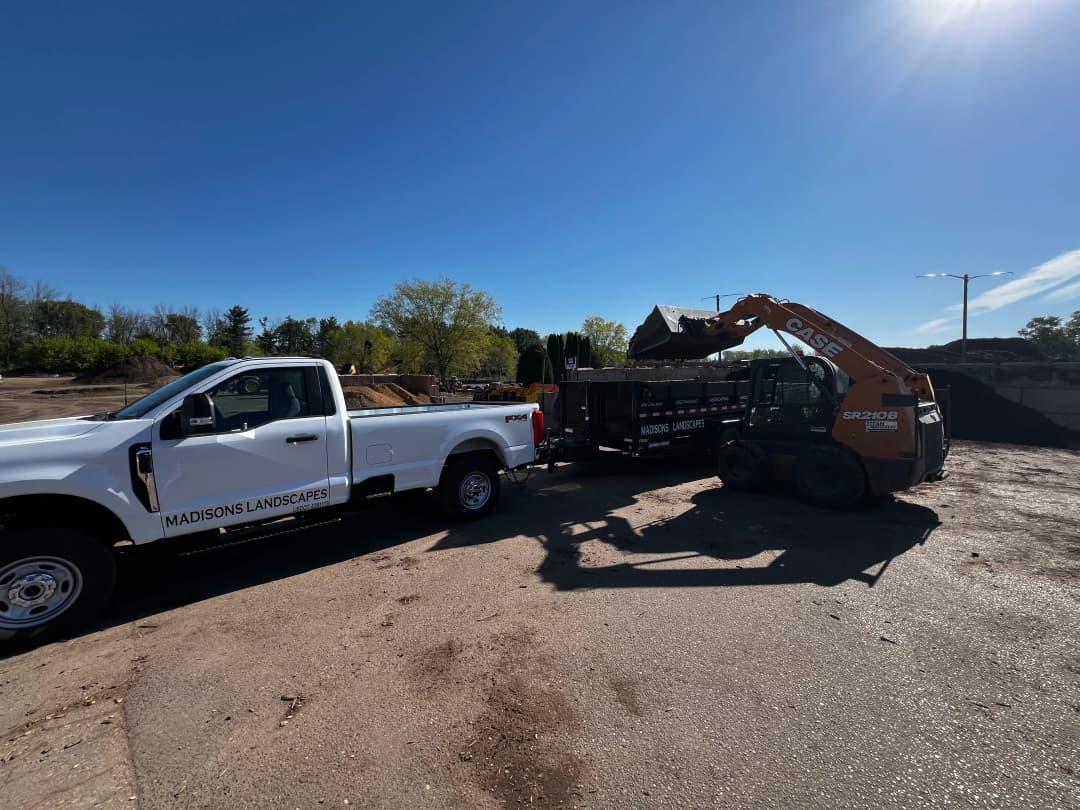 Landscaping truck and excavator working at a construction site under clear blue sky.