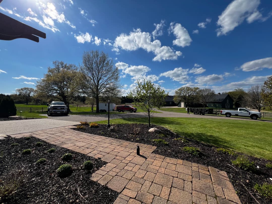 Scenic landscape with blue sky, clouds, driveway, and vehicles in a rural setting.