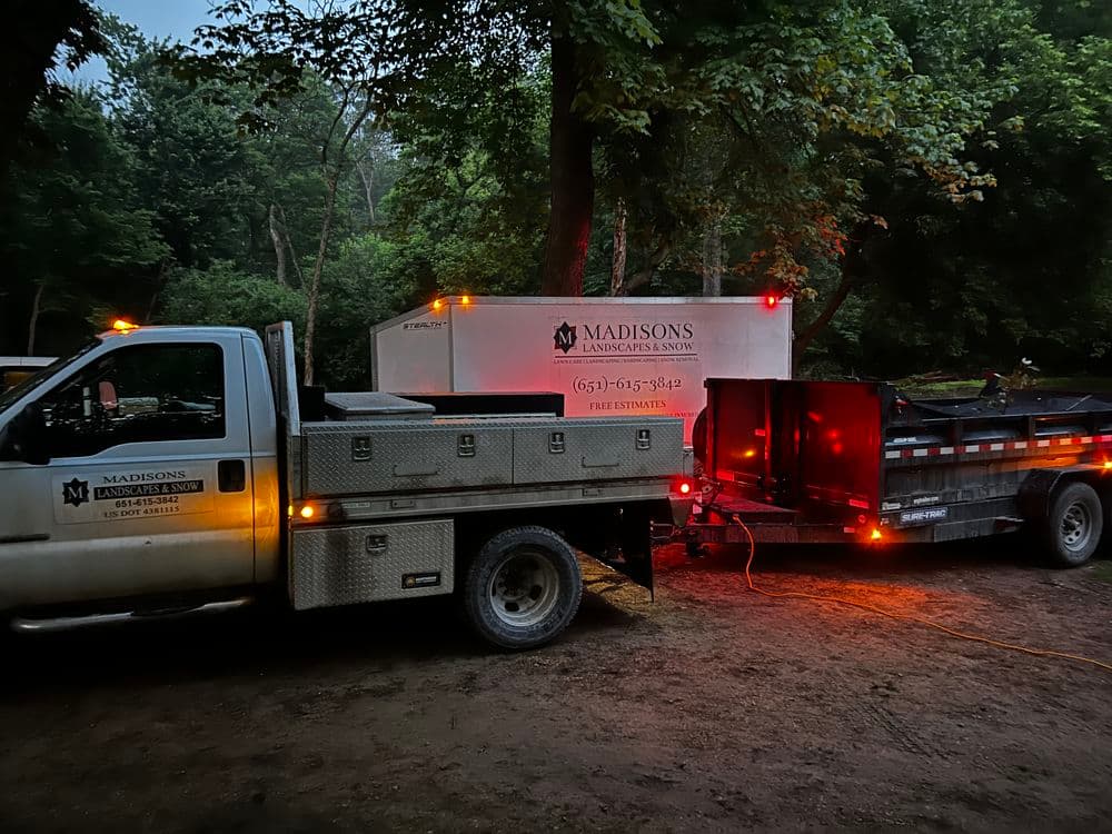 Madisons Landscaping Services truck and trailer parked in a wooded area at dusk.
