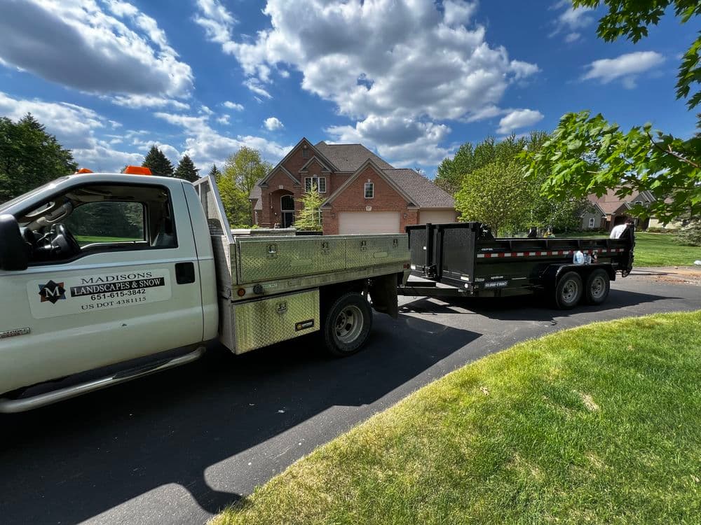 Landscape truck and trailer parked in residential driveway with a house in the background.