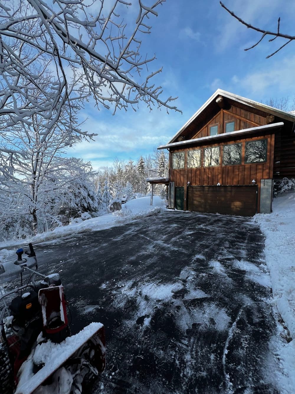 Cozy wooden mountain home surrounded by snow-covered trees and a freshly cleared driveway.