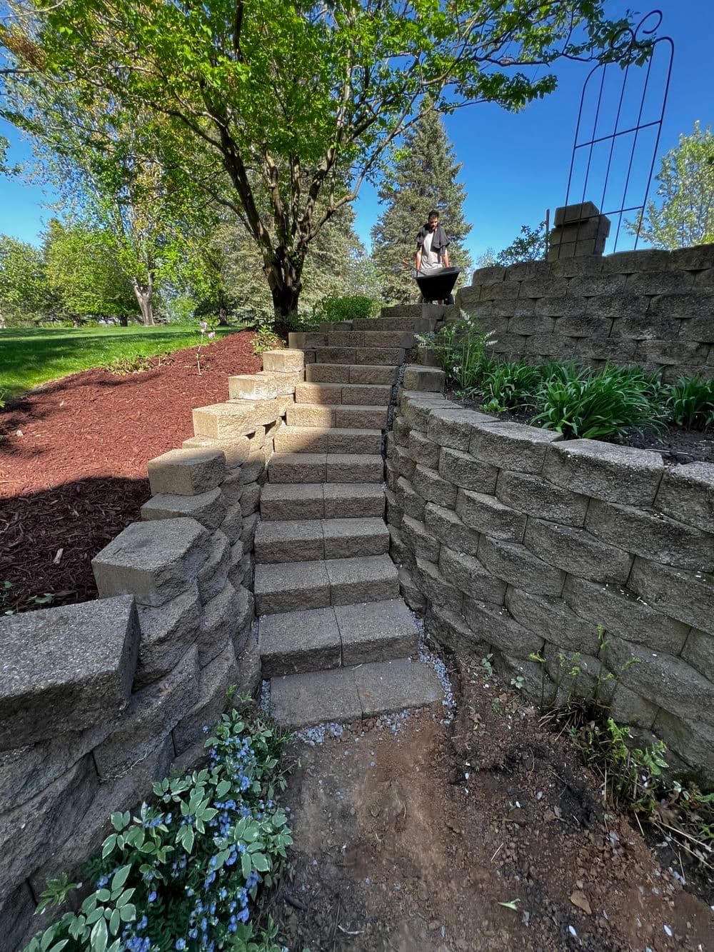 Stone steps leading up a landscaped garden with greenery and a person gardening.