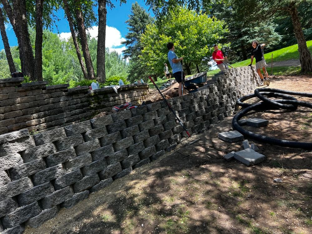 Workers building a stone wall landscape feature surrounded by trees and greenery.