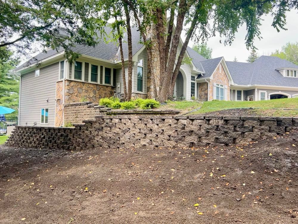 Stone retaining wall landscaping enhances a modern home with a lush garden and trees.
