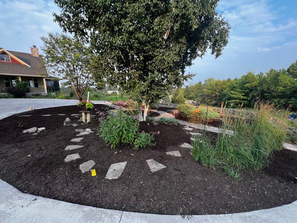 Landscape design featuring a circular garden with stepping stones, trees, and diverse plants.