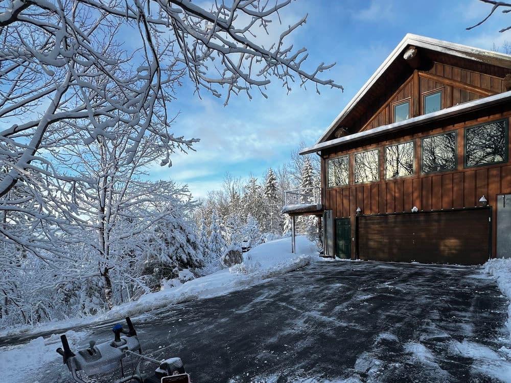 Winter landscape featuring a cozy wooden house surrounded by snow-covered trees.